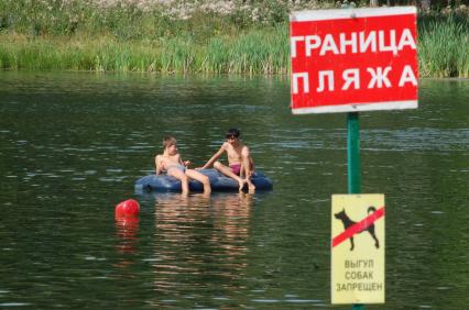 Мальчики плавают на водном надувном матрасе. На берегу стоит табличка с надписью: `Граница пляжа` и `Выгул собак запрещен`.