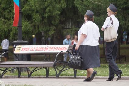 Традиционный праздник силовых структур `Служба дни и ночи` в Екатеринбурге. На снимке: женщина в полиции, две женщины идут по улице мимо скамейки с надписью: `живи по полной программе!`