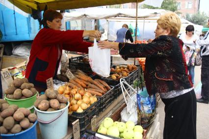 Женщина покупает продукты на овощном рынке.