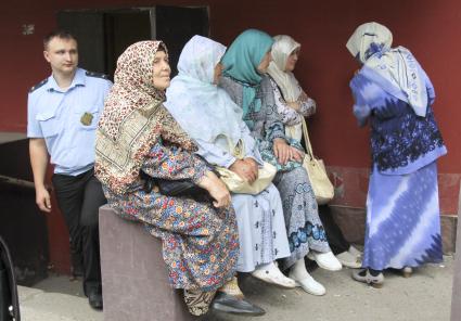 Мусульманки в хиджабах сидят у здания суда, из здания выходит судебный пристав.