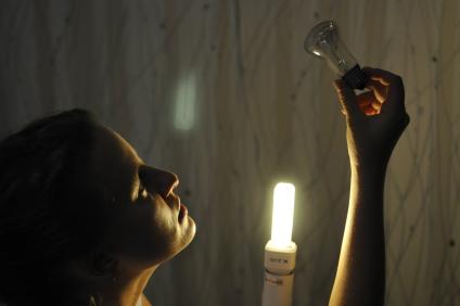 Девушка держит в руках две лампы: энергосберегающую и лампочку накаливания.
