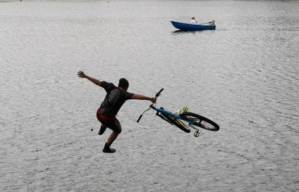 В калининградской области прошло соревнование по прыжкам в воду на велосипеде. На снимке: фаза прыжка, мимо проплывают люди в лодке.