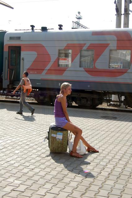 Девушка сидит на перроне вокзала с чемоданом.