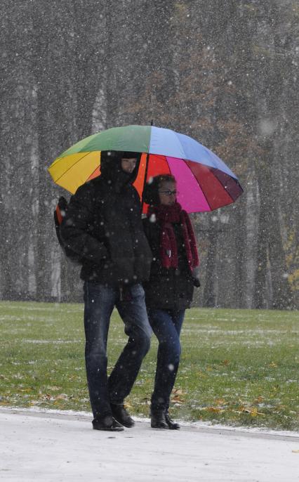Молодая пара идет под зонтом в цвет радуги. Идет первый снег.
