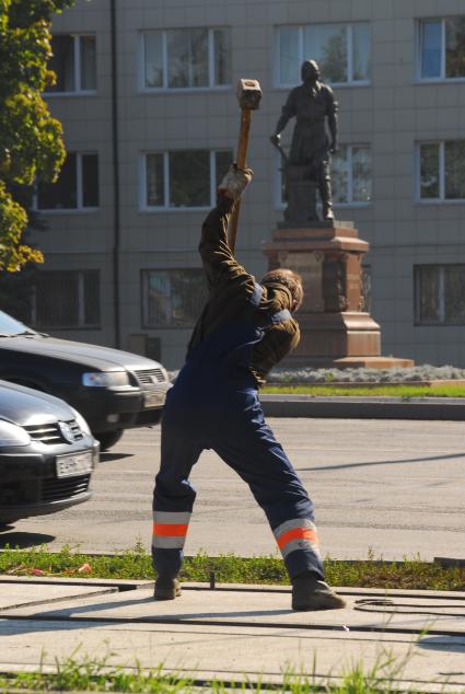 Дорожный рабочий с кувалдой на фоне памятники Петру I у Тульского оружейного завода.