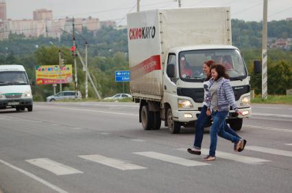 Две девушки перебегают автомобильную дорогу по пешеходному переходу.