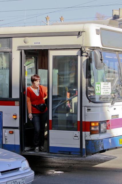 Женщина водитель общественного транспорта перекуривает в открытых дверях стоя в пробке на дороге.