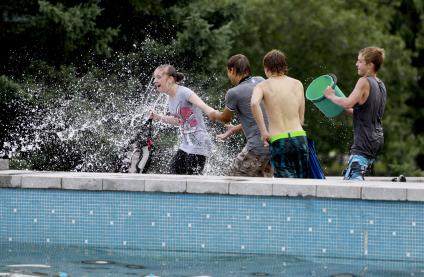 Подростки обливают водой девушку у фонтана.