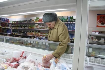 Женщина выбирает курицу в социальном магазине для пенсионеров.