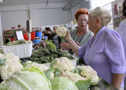 Женщины выбирают капусту на рынке в ряду торговцев овощами.