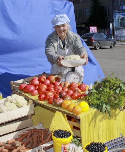 Женщина торгует овощами на открытом рынке.