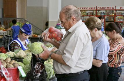 Покупатель покупает капусту и помидоры на рынке в ряду торговцев овощами.