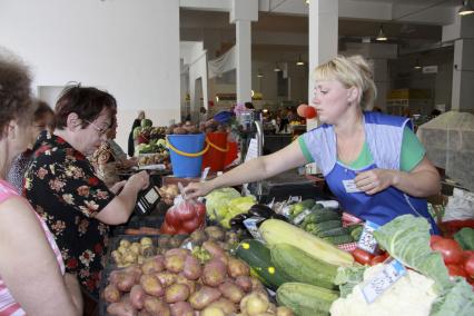 Торговля овощами на рынке. Продавец передает покупателю пакет с помидорами.