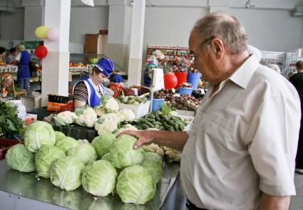 Покупатель присматривается к капусте на рынке в ряду торговцев овощами.