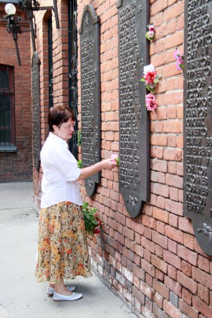 Мемориальная стена с фамилиями, женщина втыкает в стену цветок.