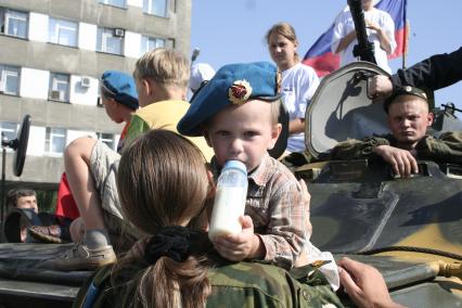 Мальчик в берете десантника пьет молоко из бутылки с соской.