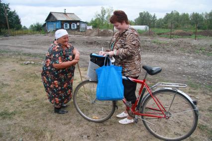 Почтальон на велосипеде разговаривает с женщиной в деревне.