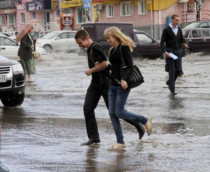 Пешеходы переходят улицу по лужам после ливня.