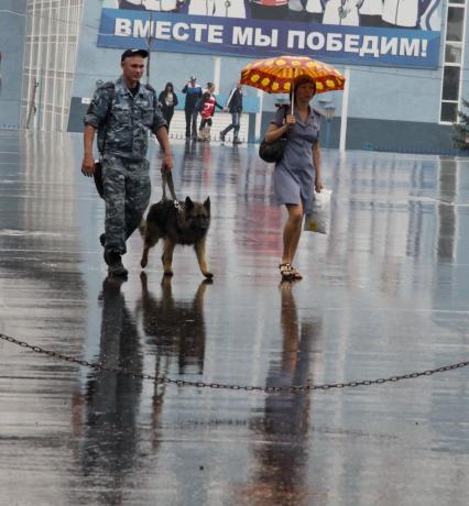 Кинолог с собакой и женщина в полицейской форме под дождем на фоне надписи: `Вместе мы победим`.