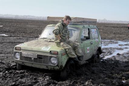 Автомобиль `Нива` застрял в поле. Водитель курит сидя на капоте.