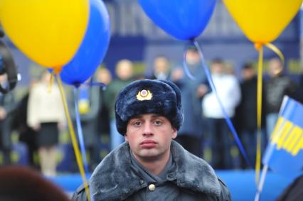 Полицейский стоит в оцеплении на митинге партии `ЛДПР`, рядом с ним висят воздушные шарики.