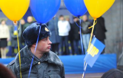 Полицейский стоит в оцеплении на митинге партии `ЛДПР`, рядом с ним висят воздушные шарики.