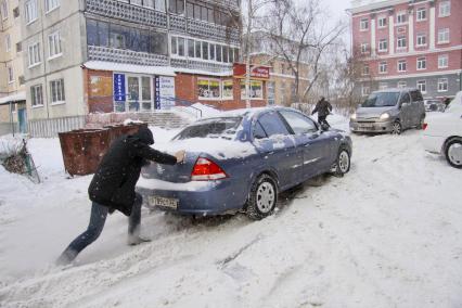 Мужчина толкает застрявший в снегу автомобиль.