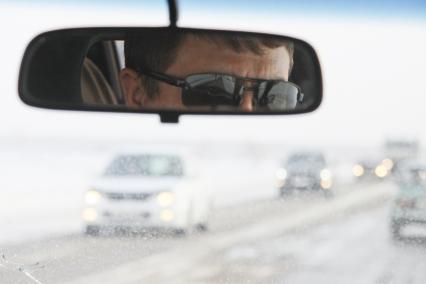 Автомобили на трассе через лобовое стекло автомобиля, в зеркале заднего вида отражения водителя в солнцезащитных очках.