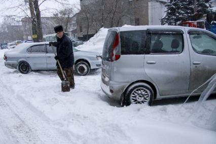 Мужчина откапывает автомобиль после обильного снегопада.