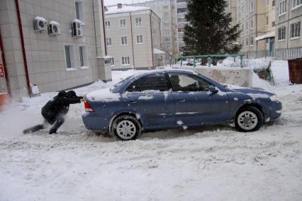 Мужчина толкает застрявший в снегу автомобиль.