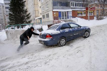 Мужчина толкает застрявший в снегу автомобиль.