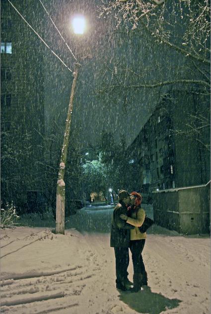 Мужчина и женщина целуются на улице под снегопадом.