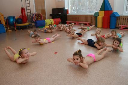 Занятия гимнастикой в детском саду. Дети выполняют упражнения лежа на полу.