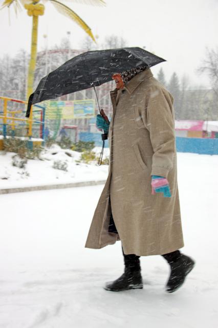 Бабушка идет под зонтом во время снегопада.