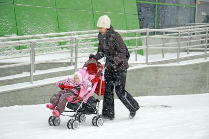 Женщина с детской коляской в городе во время снегопада.