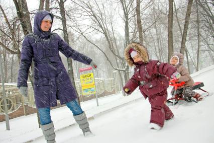 Женщина с детьми катается на горке во время снегопада.