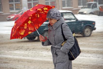 Женщина идет по городу под зонтом во время снегопада.