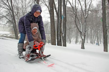 Женщина катается с горки на снегокате с ребенком во время снегопада.