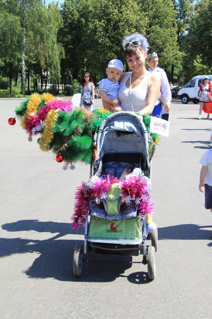 Парад детских колясок в Уфе. На снимке: мама с ребенком на руках рядом с детской коляской с новогодней елкой.