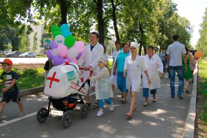 Парад детских колясок в Уфе. На снимке: родители в белых медицинских халатах идут рядом с детской коляской похожей на машину скорой помощи.