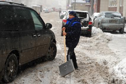 Дворник гастарбайтер чистит улицу от снега.