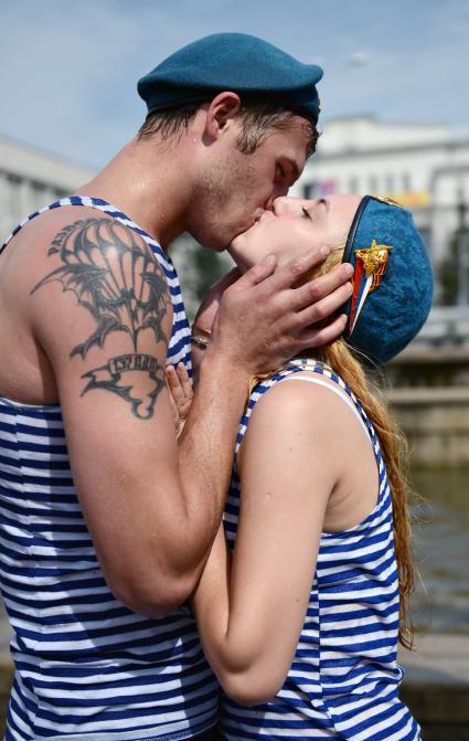Мокрые мужчина и женщина в тельняшках и беретах десантника целуются у фонтана.