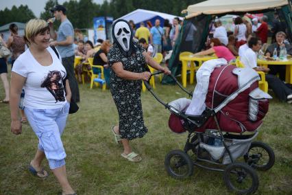 Современная бабушка в маске из фильма `Крик` везет ребенка в детской коляске.