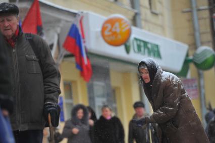 Женщина с протянутой рукой просит милостыню на улице у прохожих людей.