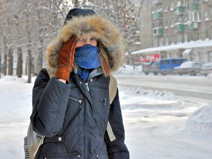 Девушка идет по заснеженной улице пряча лицо от мороза.