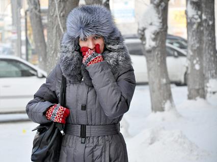 Девушка идет по заснеженной улице пряча лицо от мороза.
