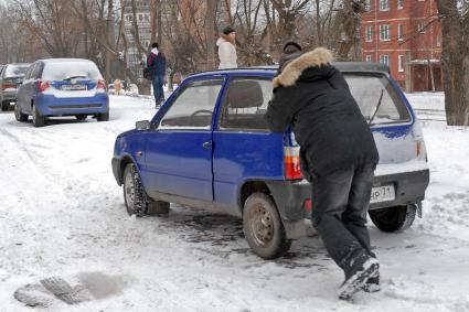 Мужчина толкает автомобиль `Ока`.