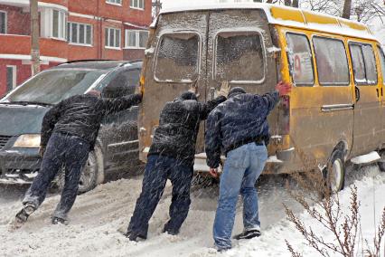 Мужчины толкают маршрутку застрявшую в сугробах.