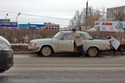 Мужчина и женщина толкают поломанный автомобиль ГАЗ.