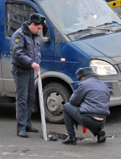 Два сотрудника ГИБДД измеряют метром глубину ямы на проезжей части.